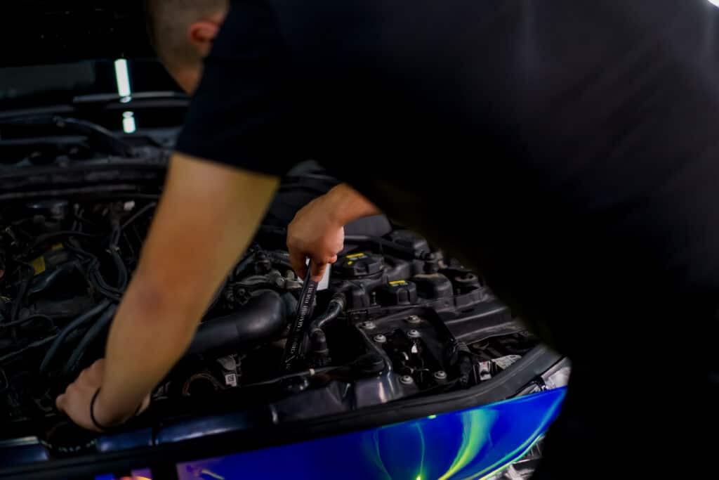 A car service worker with a wrench in his hands fixes a car in chamillion-colored film with the hood open